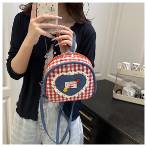 Mirror selfie showing a small red plaid canvas backpack with a denim heart and cherry tag