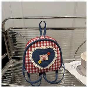 Detail of red plaid backpack with denim heart patch and cherry embroidery on metal shelf