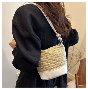 Detail of woven straw bucket bag with white leather straps and trim on a model