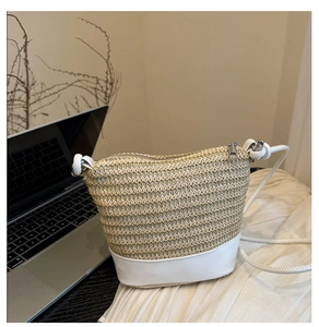 Detailed view of woven straw bucket bag with white faux leather base and zipper closure