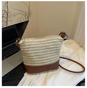 Close-up of handwoven straw bucket bag with brown faux leather base and zipper detail