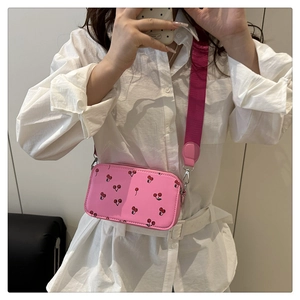 Pink shoulder bag with cherry print and wide strap shown in a mirror selfie