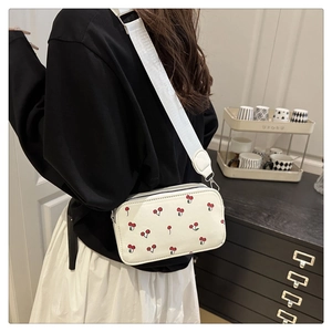 Detailed close-up of a white leather crossbody bag with cherry print and wide strap