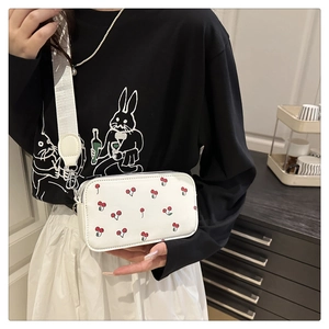 Detailed view of white cherry print crossbody bag with wide nylon strap and silver zippers