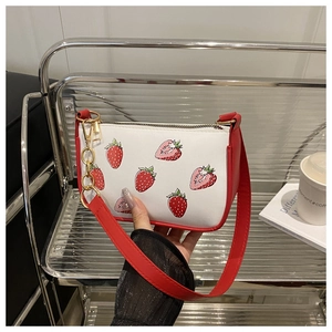 Détail d'un sac bandoulière rouge et blanc avec imprimé fraise et chaîne dorée