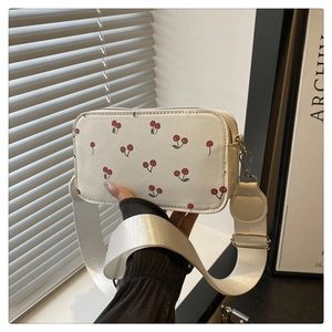 Detail of white camera bag with red cherry prints and wide fabric shoulder strap