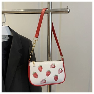 Detail of red strawberry print on white shoulder bag with gold metal chain strap