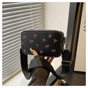 Close-up of black rectangular crossbody bag featuring red cherry print and wide strap