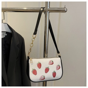 Close-up of a white baguette bag featuring sweet strawberry prints and black shoulder strap