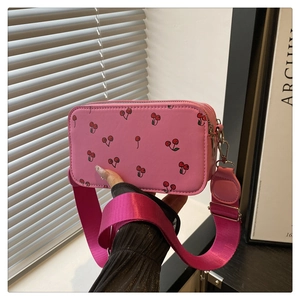 Detail of pink cherry print crossbody bag featuring a wide magenta nylon shoulder strap