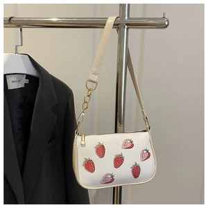 Detail of a creamy white underarm bag with vivid strawberry prints and golden chain strap