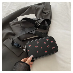 Close-up of black PU leather crossbody bag with red cherry print and wide strap