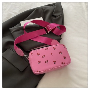 Detailed top view of pink cherry print crossbody bag with wide strap on grey suit fabric