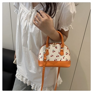 Detail of cherry print shell bag featuring bright orange leather straps and gold zippers