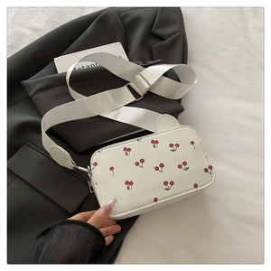 Close-up of white cherry print crossbody bag with adjustable wide strap on grey blazer
