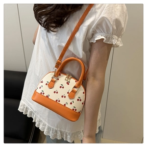 Detailed view of cherry print shell bag with orange straps worn as a crossbody purse