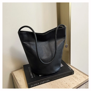 Close-up of black lychee grain tote bag with silver chain charm on elegant book stand