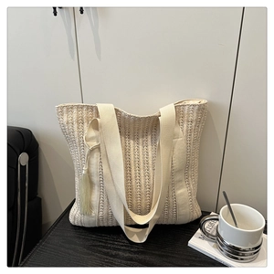 Detail view of woven beige tote bag featuring canvas straps and a stylish tassel charm