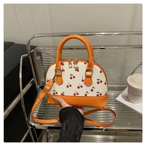 Detailed view of cherry print shell bag with orange leather handles and gold metal zippers