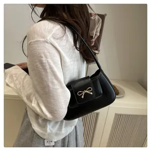 Detailed view of black underarm bag with golden bow buckle and matte leather texture