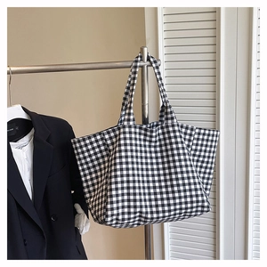 Detail of a black and white checkered canvas tote bag on a metal hanger with suit