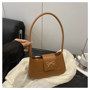 Detail of a brown faux leather shoulder bag featuring a golden bow metal buckle on a silk base