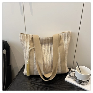 Detail of minimalist straw tote bag featuring long tassels and woven vertical stripes