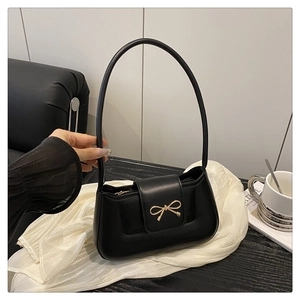 Detail of black PU leather hobo bag with gold bow clasp on white silk background