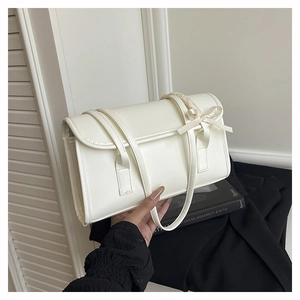 Détail d'un sac à main blanc en cuir avec nœud en soie sur la anse et rabat élégant