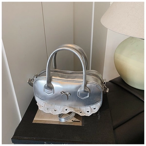 Detail der silbernen Metallhandtasche mit Schleifenanhänger und weißem Spitzenbesatz unten
