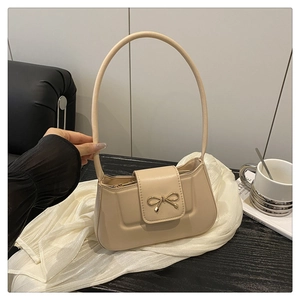 Detailed close-up of cream leather shoulder bag with golden bow clasp on black table