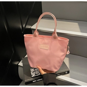 Detailansicht der pinkfarbenen Nylon-Minitasche mit FASHION-Label vor urbanem Design