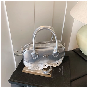 Detail einer silbernen Handtasche aus PU mit zarter Metallschleife und Spitzenbesatz am Boden
