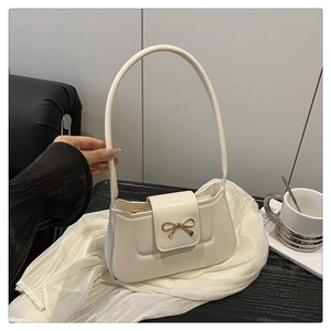 Detail of cream-white bow clasp shoulder bag on table with coffee cup accessory