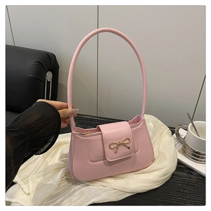 Close-up of a pink shoulder bag featuring a gold metal bow and sleek leather texture
