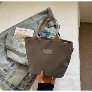 Detail der dunkelgrauen Nylon-Minihandtasche mit FASHION-Label auf modernem Hintergrund