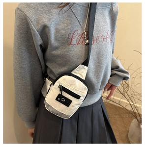 Close-up of white nylon crossbody bag featuring black zipper and mesh detail on model