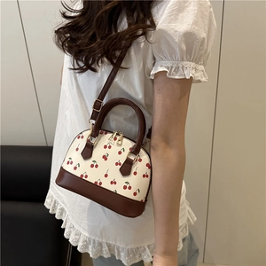 Chic shell bag with red cherry print and brown leather trim worn as a crossbody bag