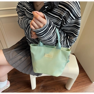 Nahaufnahme der minzgrünen Nylon-Handtasche mit FASHION-Label, gehalten von Model