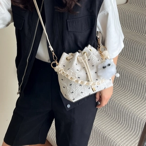 Sac seau blanc avec motifs nœuds noirs, fermeture à cordon et breloque monstre en peluche
