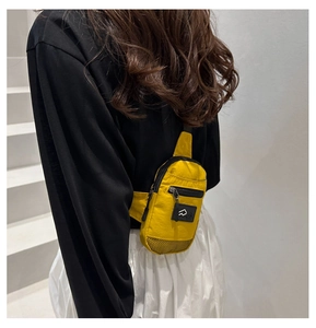 Detail of a bright yellow nylon chest bag with black mesh trim and a minimalist logo tag