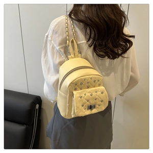 Detail of light yellow quilted mini backpack with rivets and metal chain straps