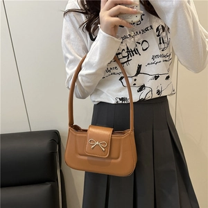 Caramel brown handbag with gold bow buckle clasp shown as a stylish crossbody bag