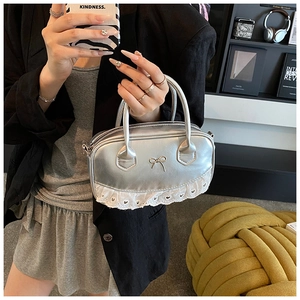Detailansicht der silbernen Mini-Handtasche mit Metallelementen und weißem Spitzenbesatz