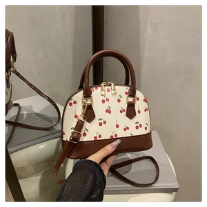Detailansicht der cremefarbenen Kirschmuster-Tasche mit braunen Ledergriffen und Golddekor
