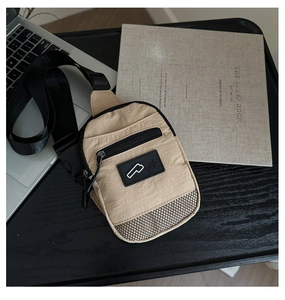 Detail of beige nylon crossbody bag featuring MX logo, mesh pocket, and black wide strap