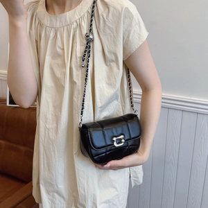 Quilted black chain crossbody bag with silver sphere detail shown on model in soft light