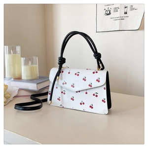 Gros plan sur l'imprimé cerises et les poignées noires du sac à bandoulière blanc