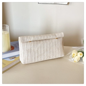 Detail of cream woven straw envelope clutch with metal clasp and textured pattern