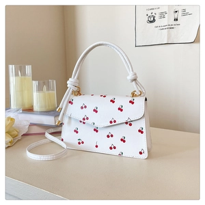 Détail du sac à bandoulière en cuir blanc avec motifs cerises et boucles dorées